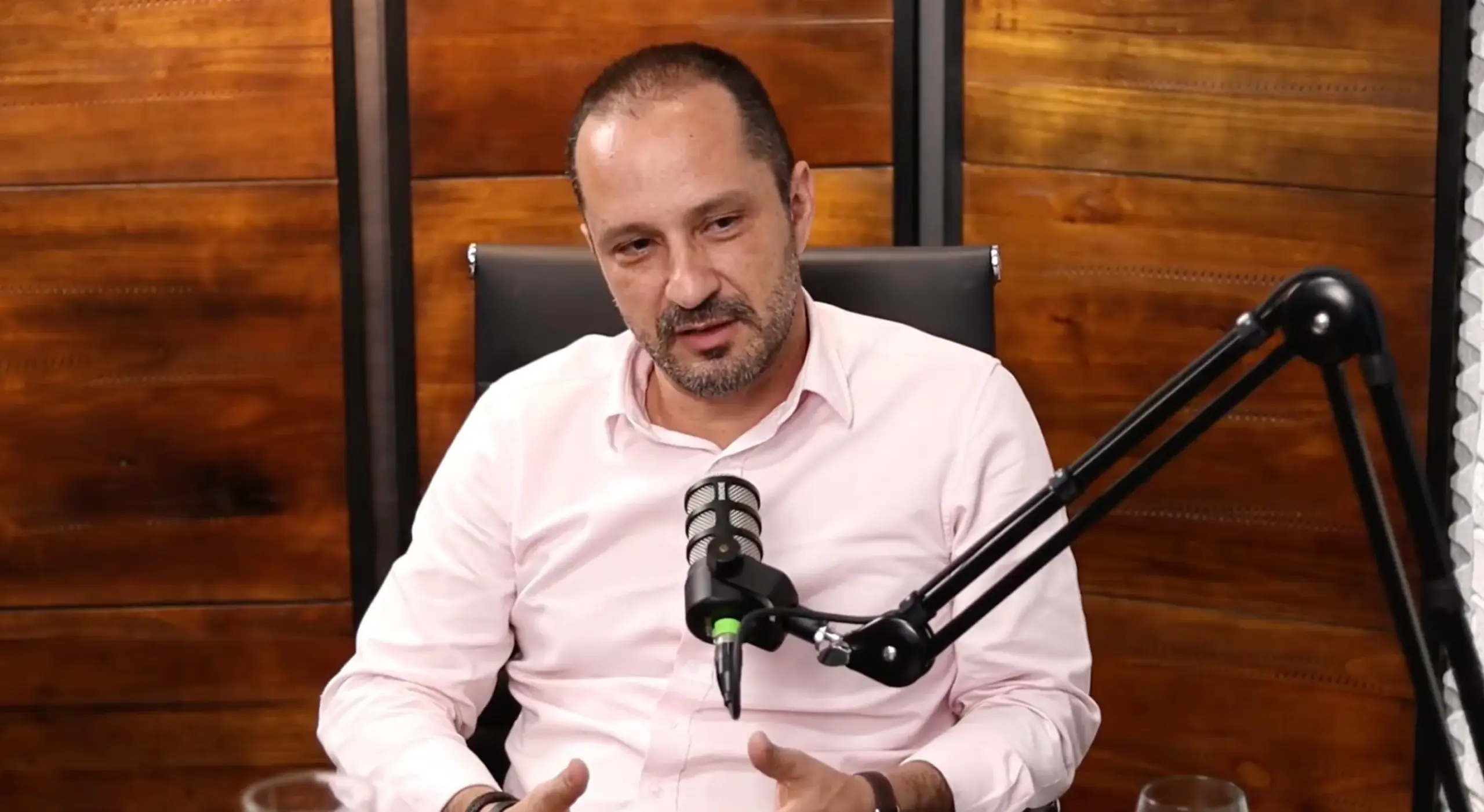 Homem fala ao microfone em estúdio de podcast.