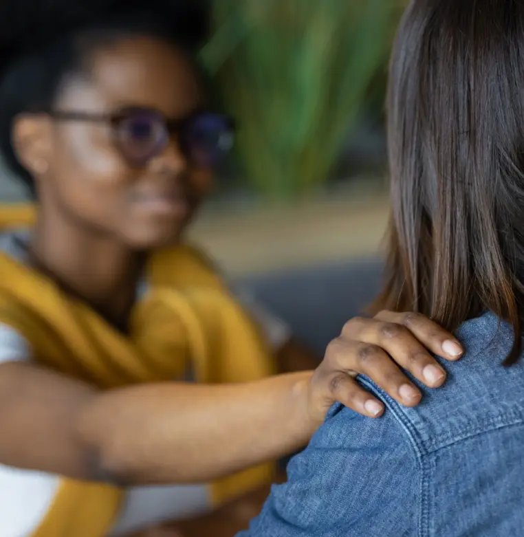 mulher dando suporte a outra no ambiente de trabalho Duas mulheres de frente uma para a outra: uma consola a outra, com a mão apoiada no ombro.